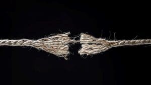 Frayed rope about to break on black background concept for stress, risk, problem, fragility or precarious business situation