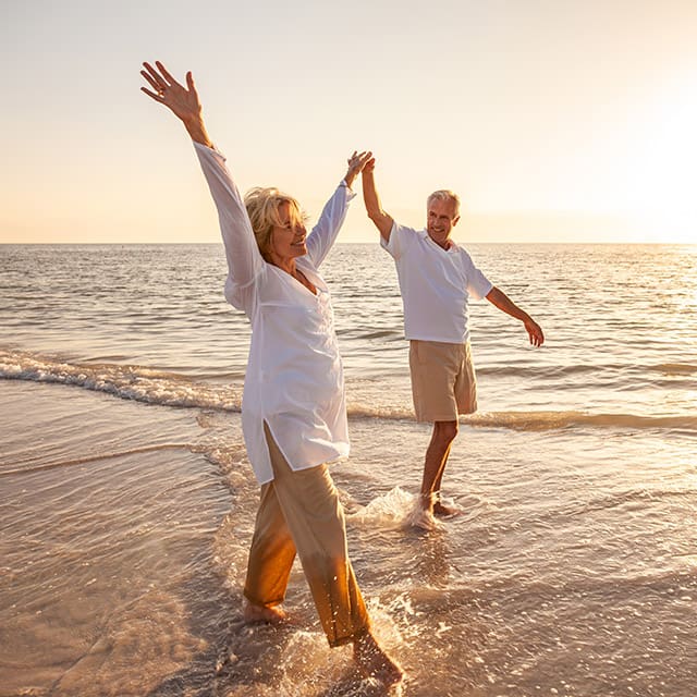 Older couple raising hands on beach at sunset
