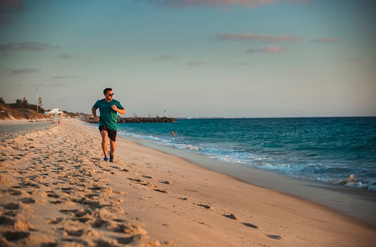 A front-view shot of a caucasian mid-adult man jogging across the beach on a hot summer's day in Perth, Australia.