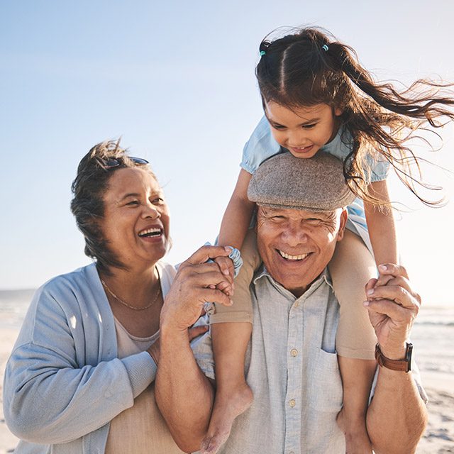 Grandparents with granddaughter on sunny beach with wind blowing their hair