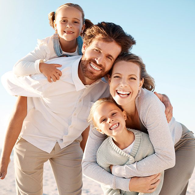 Family with 2 children posing together on the beach in the sun