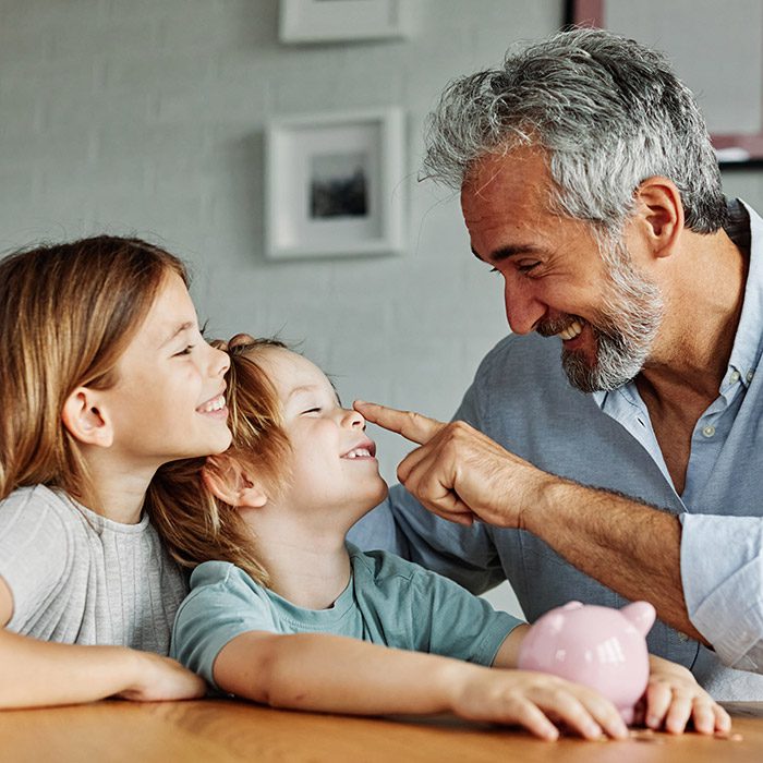 Grandparent grandfather And His Grandson and granddaughter Putting Coin Money In Piggybank At Home. Personal Savings, Bank Safety And Financial Investments Concept