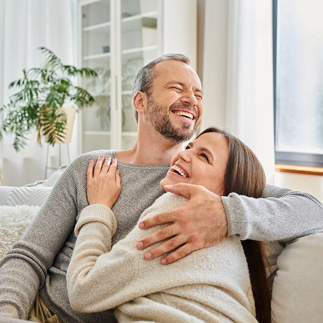Couple embracing and laughing on couch in modern living room, calm lifestyle