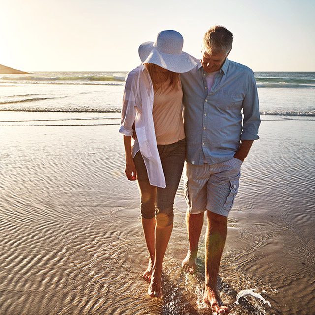 Senior, happy couple and walking with hug on beach sunset for love, embrace or bonding together in nature.